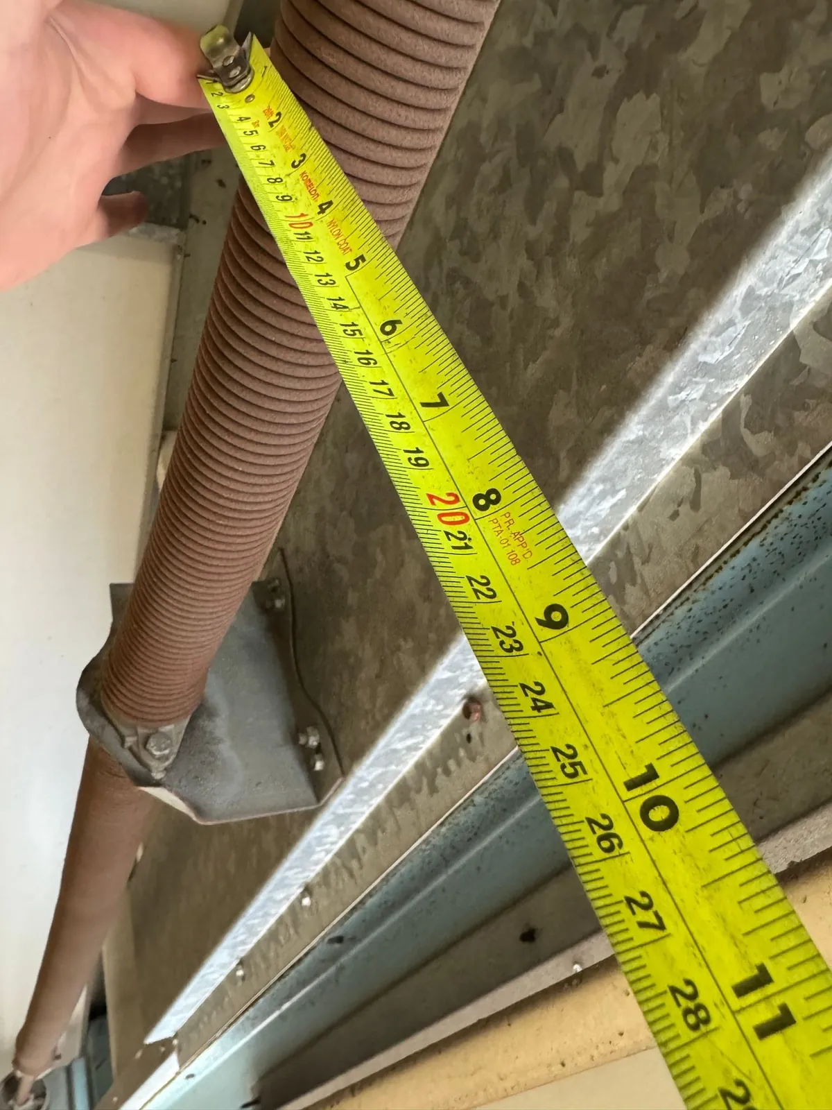 Rusted, corroded garage door torsion spring beside a tape measure — coastal salt-air wear