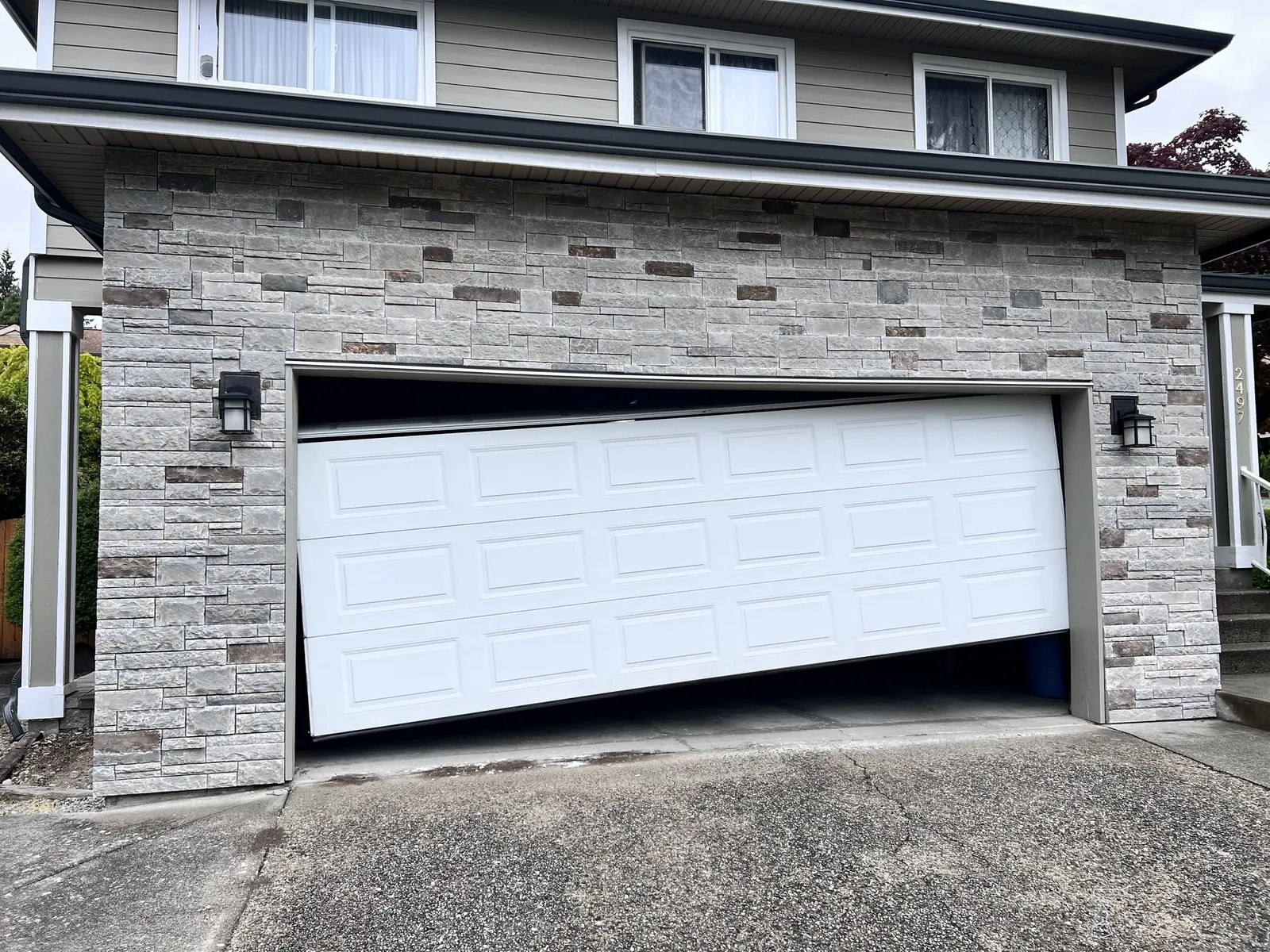 White garage door knocked off its tracks on a stone-front home in Tsawwassen Shores